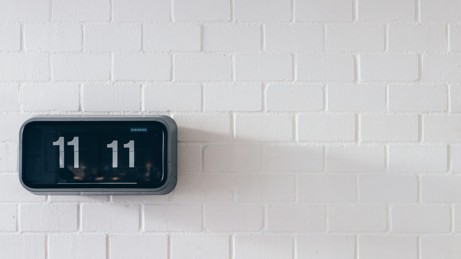 A flip clock mounted on a white wall, its cards set to 11:11.