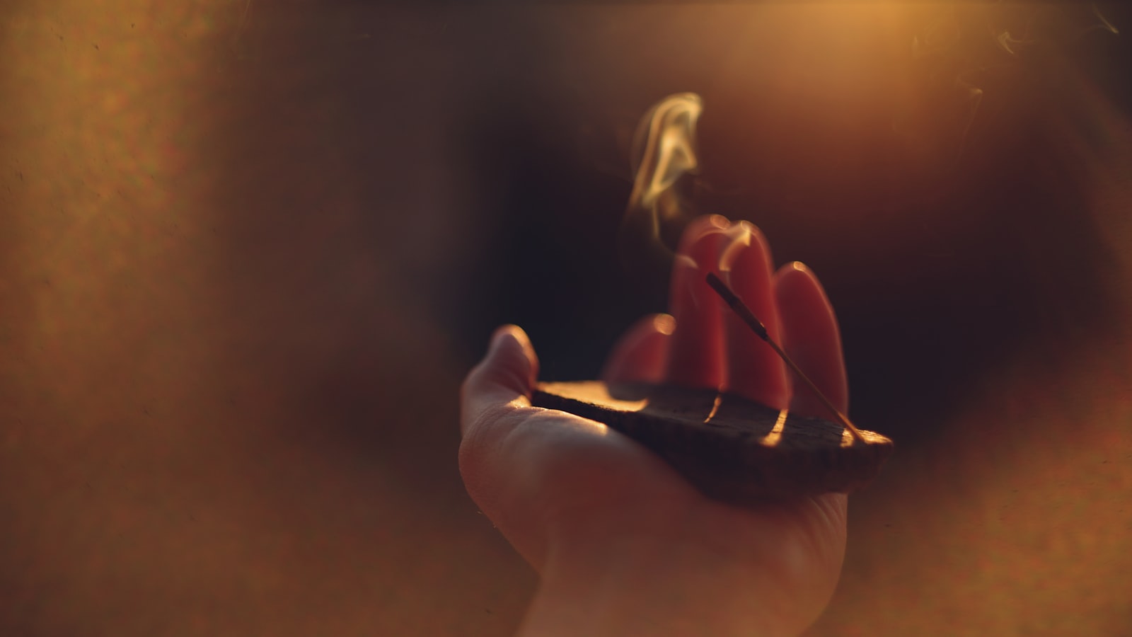 A hand holding a burning incense stick with smoke rising