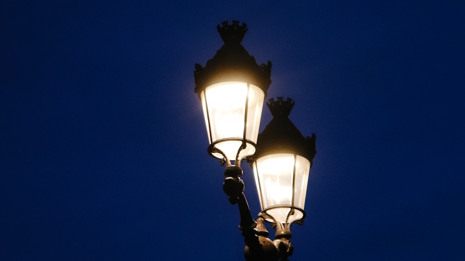 A lit double-lantern street lamp glowing against a deep dark-blue winter evening sky