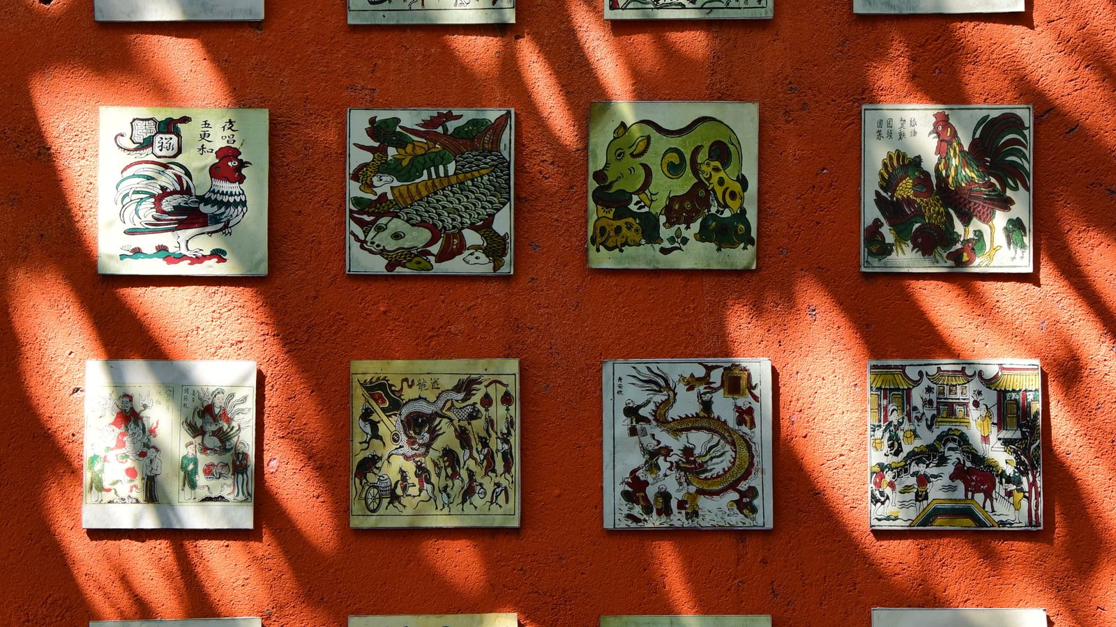 Colorful ceramic tiles painted with Chinese zodiac animals mounted on a warm orange wall.