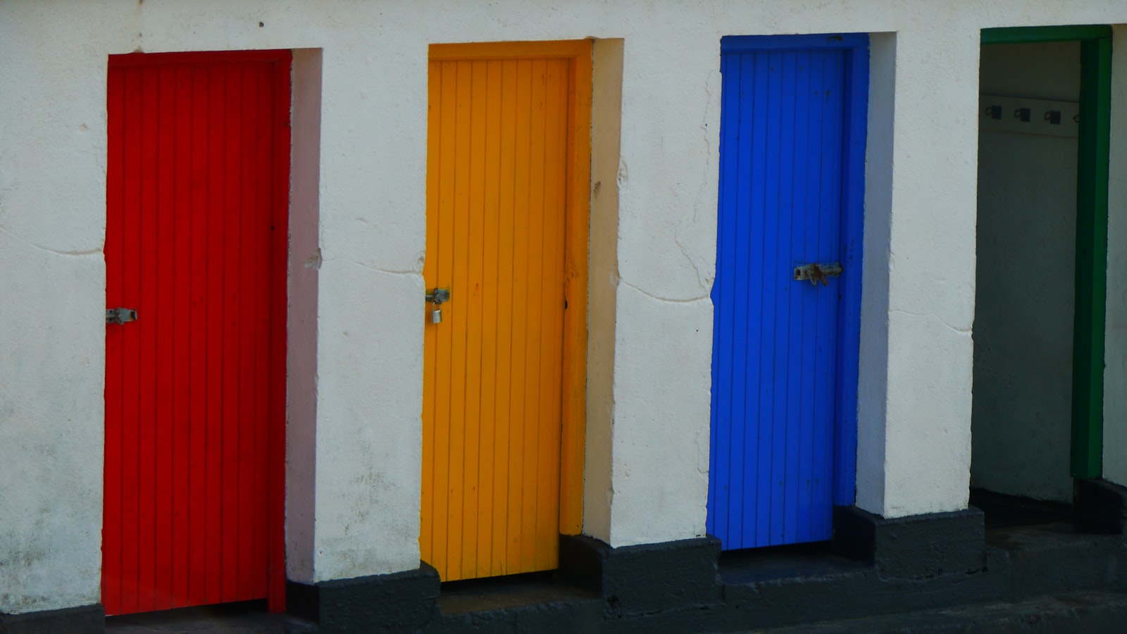 Three doorways painted red, orange and blue side by side on a whitewashed wall.