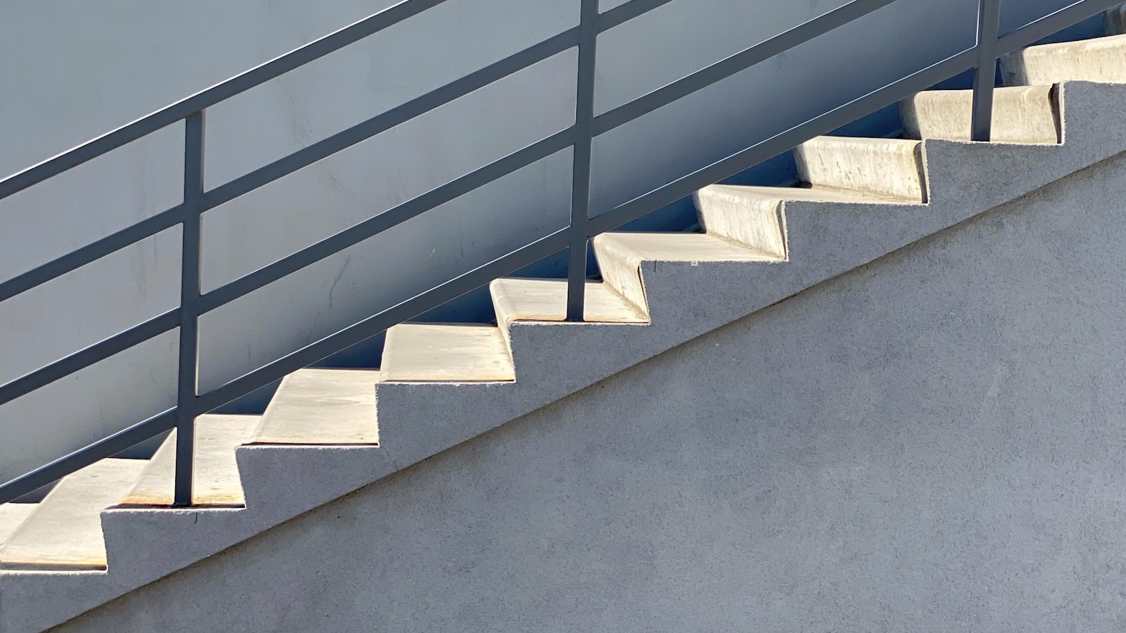 A white concrete staircase with black metal railings ascending diagonally through the frame.