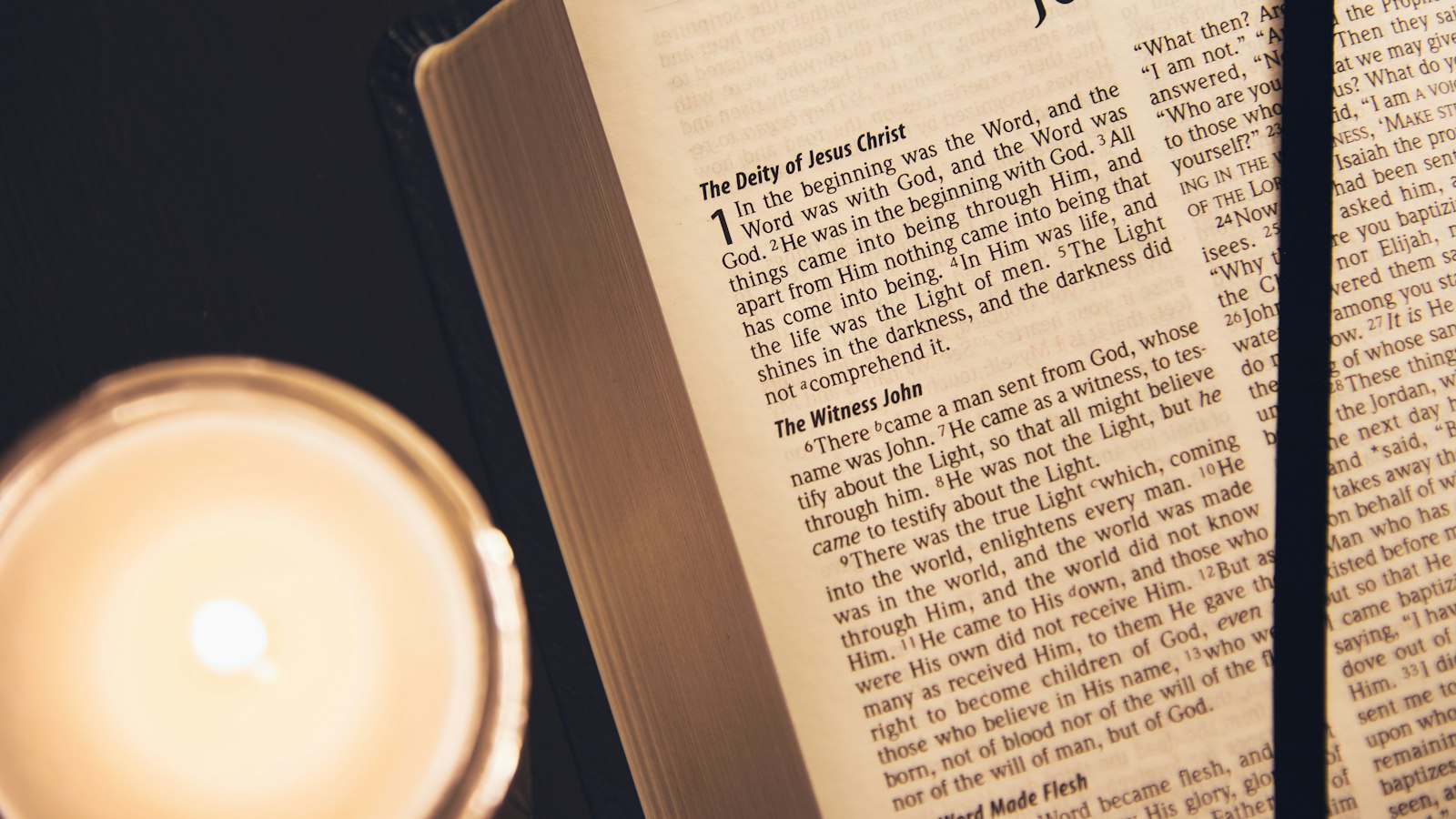 A close-up of an open Bible page with a candle flame burning against the printed words.