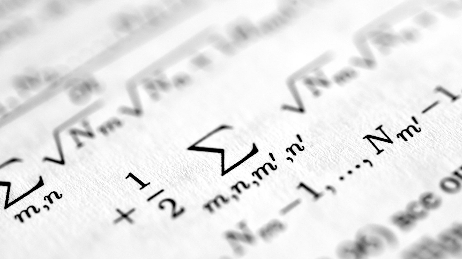 A macro photograph of handwritten equations and numbers filling a printed page, the columns nearest the lens in sharp focus and the rest dissolving into blur.