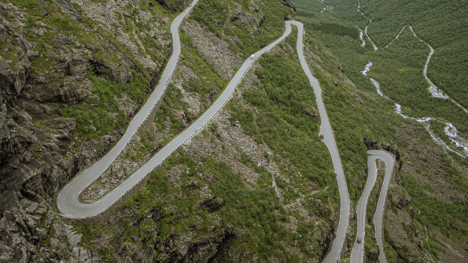Aerial view of a switchback mountain road winding down a green mountainside in tight hairpin turns