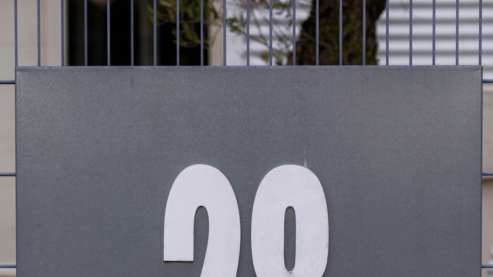 A large metal house number sign reading 28, mounted on a gray wall.