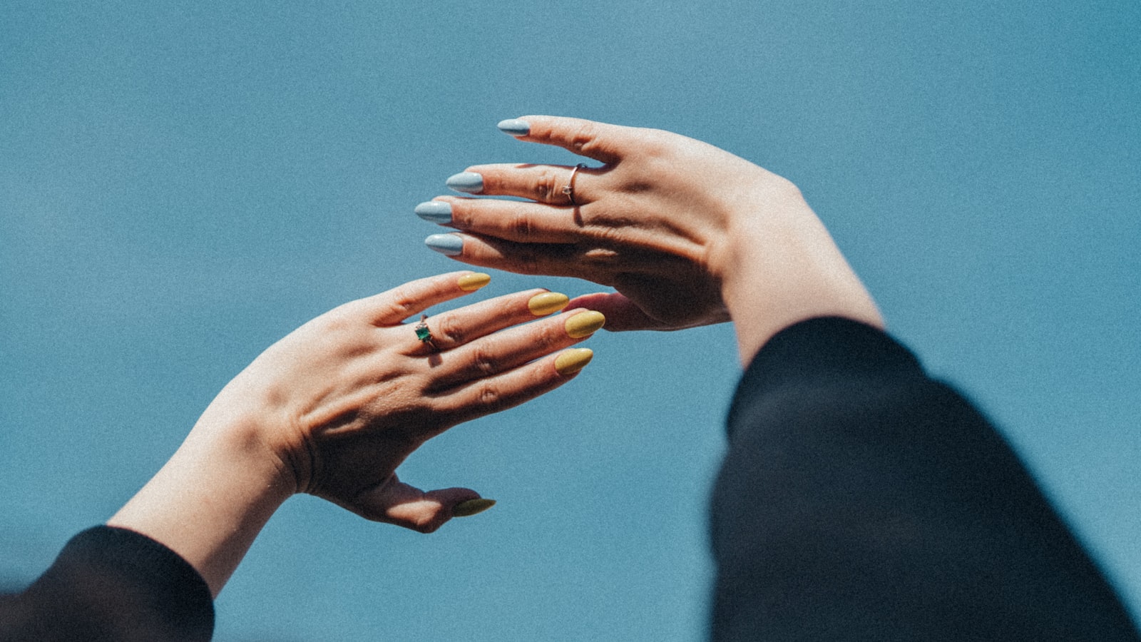 Two hands reaching toward each other against a plain background, fingertips almost touching