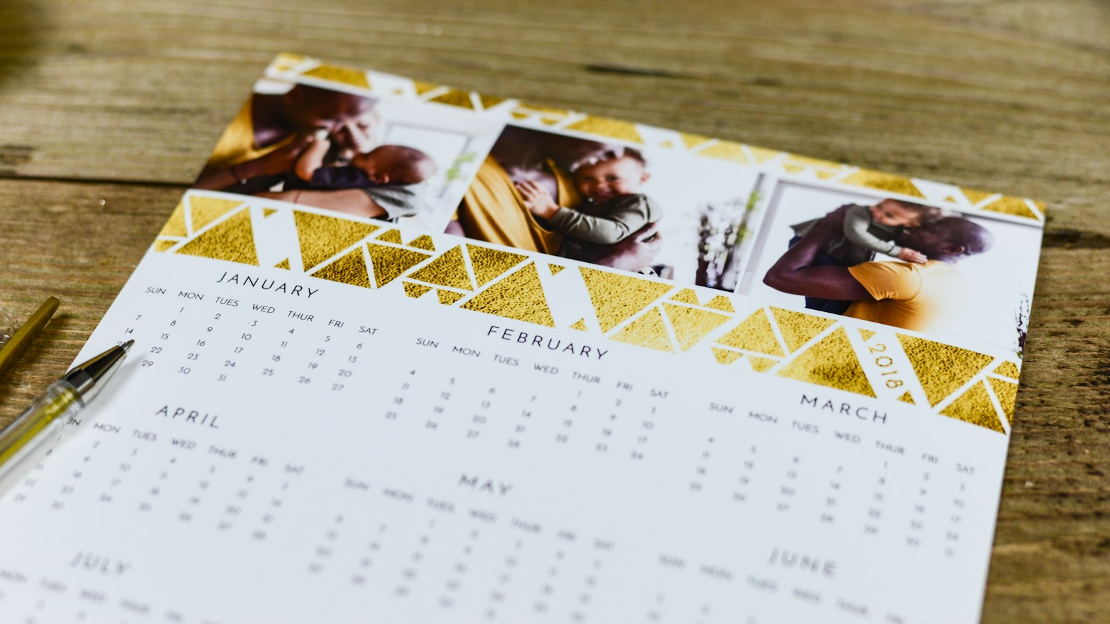 A white desk calendar with gold trim standing open on a brown surface.