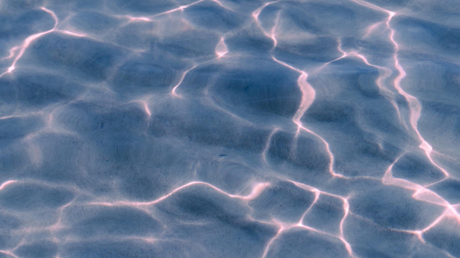 Close-up of rippling blue water with pale, thread-like streaks of sunlight refracting across the rolling surface.
