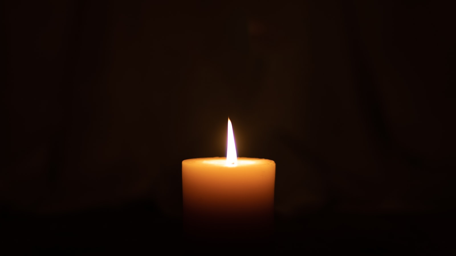 A single lit candle glowing softly in an otherwise dark, quiet room