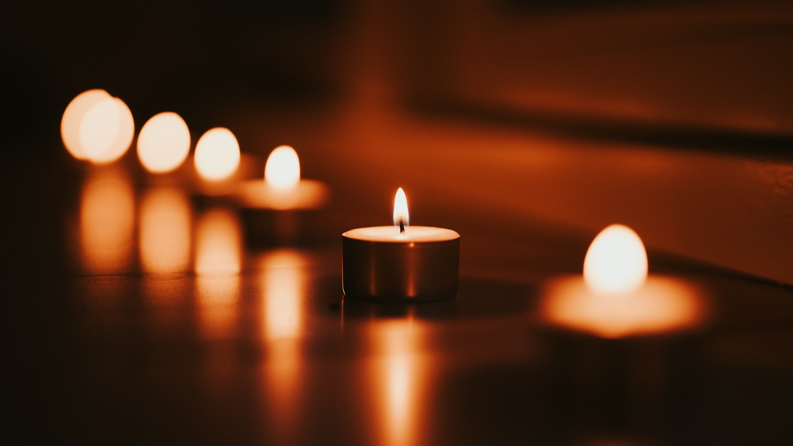 Candles glowing warmly in dim, quiet light against a dark background.